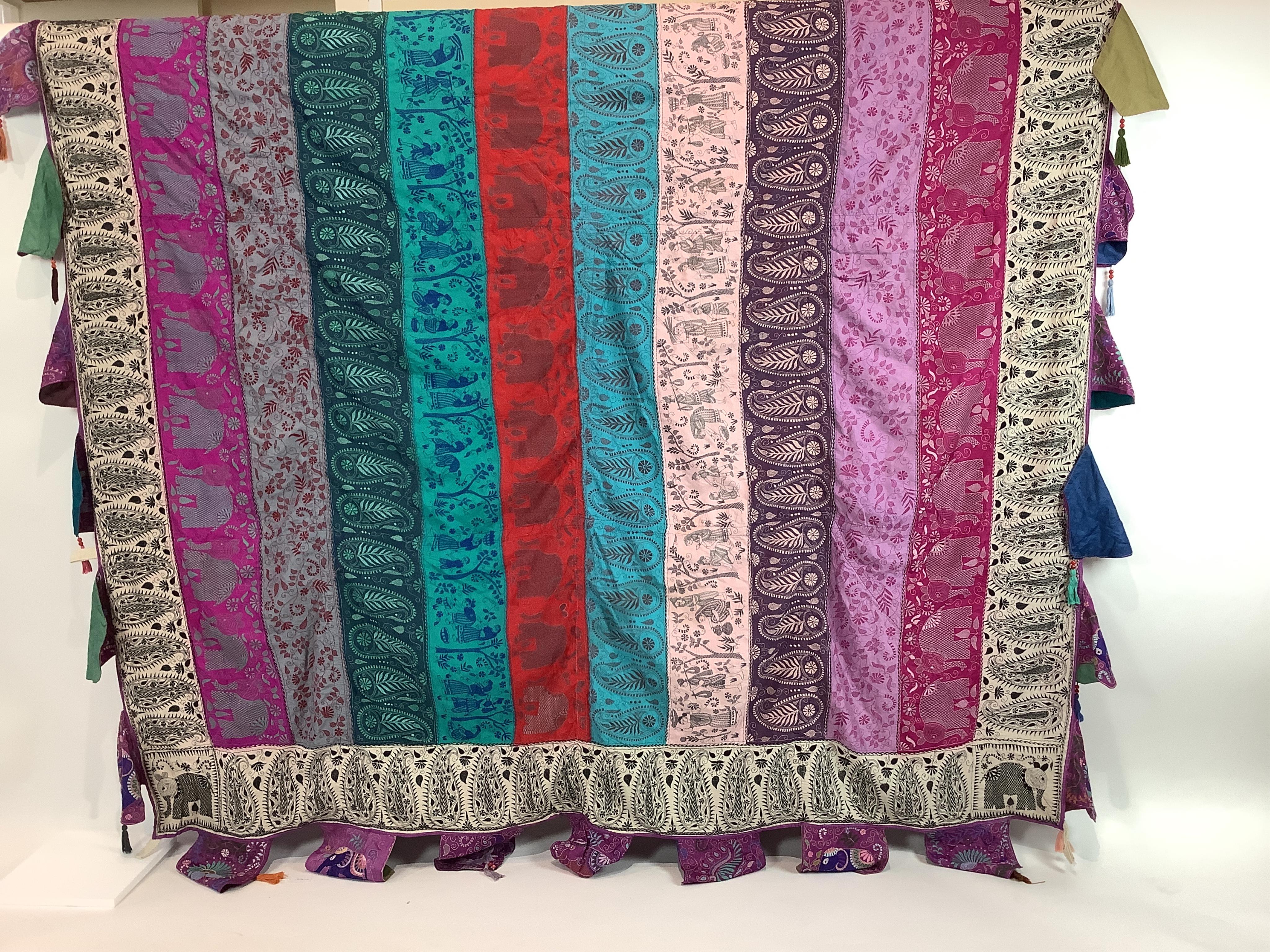 An Indian 20th century embroidered silk hanging, with decorative triangular tasselled edges. Worked in colourful silk stripes, with varying silk embroidered all over motifs. Bordered with colourful silk, beaded, tasselle